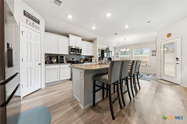 kitchen featuring stainless steel appliances, a breakfast bar, visible vents, light stone countertops, and an island with sink