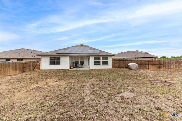 rear view of house featuring a fenced backyard, roof mounted solar panels, a lawn, and a patio