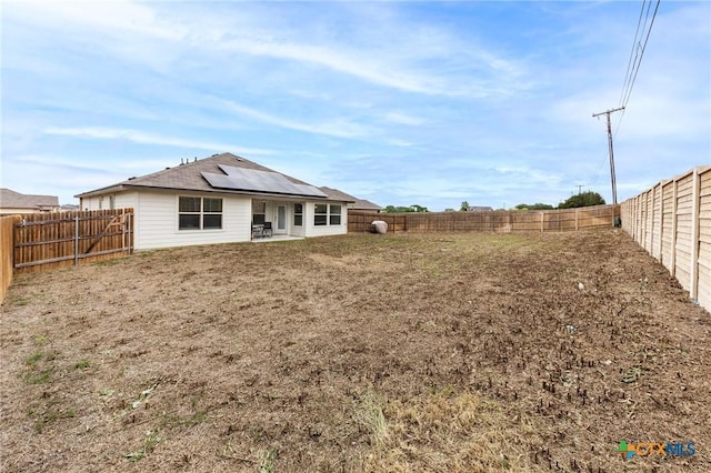 rear view of property with a fenced backyard, solar panels, and a patio