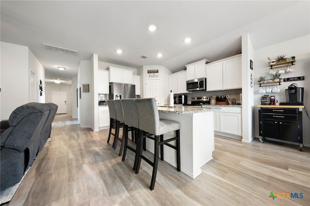 kitchen featuring appliances with stainless steel finishes, a breakfast bar area, light wood-style flooring, and visible vents