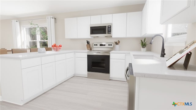 kitchen with white cabinets, a peninsula, a sink, light countertops, and appliances with stainless steel finishes