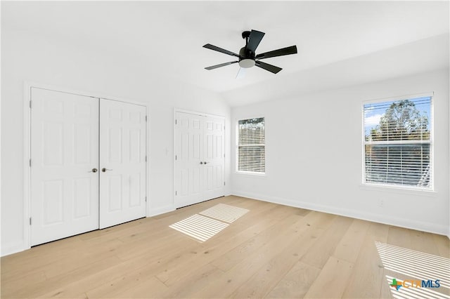 unfurnished bedroom featuring multiple windows, two closets, ceiling fan, and vaulted ceiling