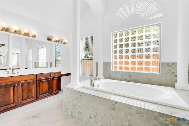 bathroom with decorative columns, a relaxing tiled tub, and vanity