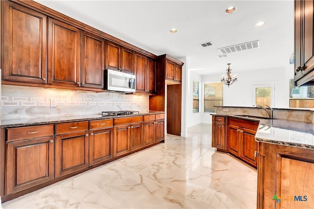 kitchen featuring a chandelier, hanging light fixtures, dark stone counters, appliances with stainless steel finishes, and sink