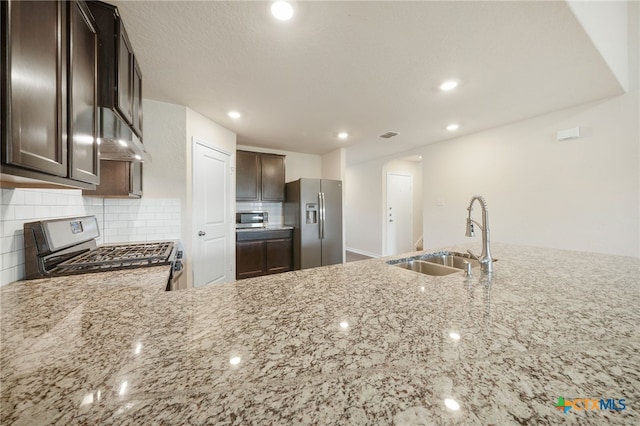 kitchen featuring sink, light stone countertops, appliances with stainless steel finishes, tasteful backsplash, and dark brown cabinets