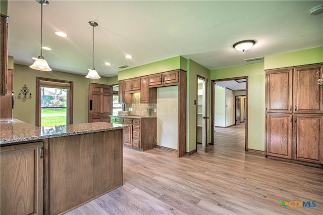 2702 Olympia Dr, Temple, TX 76502 - kitchen with dark stone countertops, light wood-style flooring, brown cabinetry, decorative backsplash, and pendant lighting