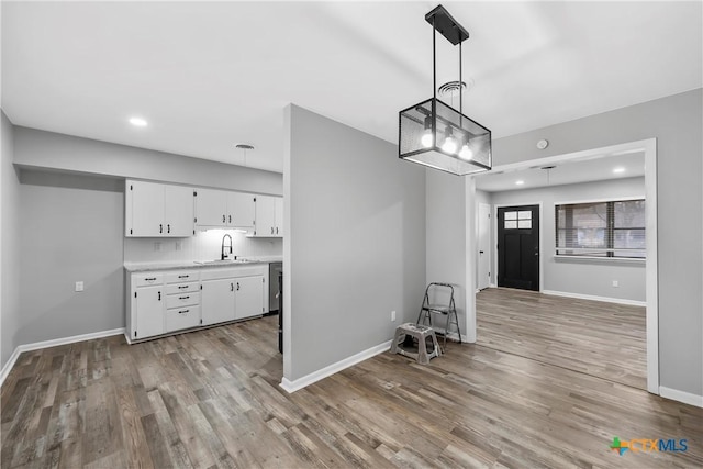 interior space featuring decorative light fixtures, light countertops, light wood-style floors, white cabinetry, and a sink