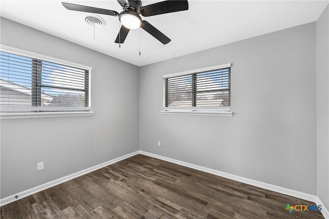 empty room featuring dark wood-style floors, visible vents, a ceiling fan, and baseboards