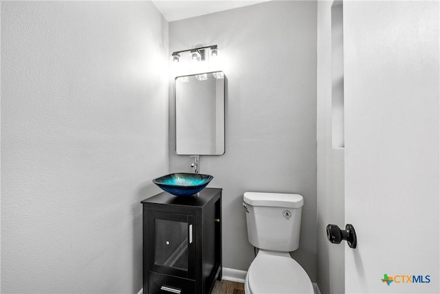 half bathroom with baseboards, vanity, and toilet