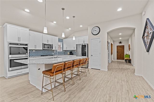 kitchen featuring a kitchen island with sink, white cabinetry, stainless steel appliances, a kitchen breakfast bar, and light stone counters