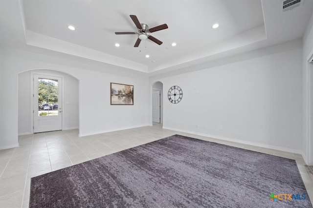 empty room featuring a tray ceiling, ceiling fan, and light tile patterned flooring