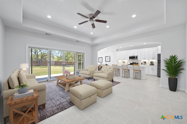 tiled living room with a raised ceiling and ceiling fan