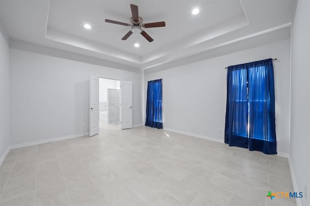 tiled empty room with a raised ceiling and ceiling fan