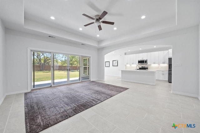 unfurnished living room featuring a tray ceiling, ceiling fan, and light tile patterned floors