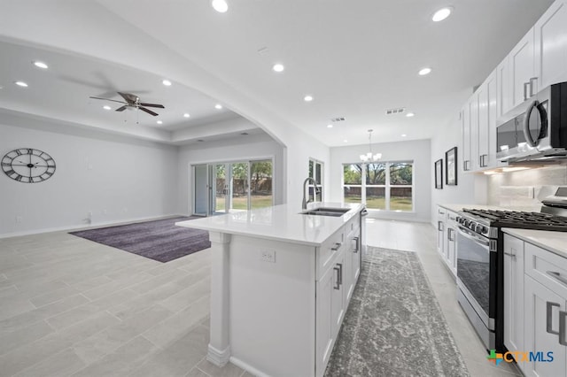 kitchen featuring a center island with sink, ceiling fan with notable chandelier, sink, appliances with stainless steel finishes, and white cabinetry