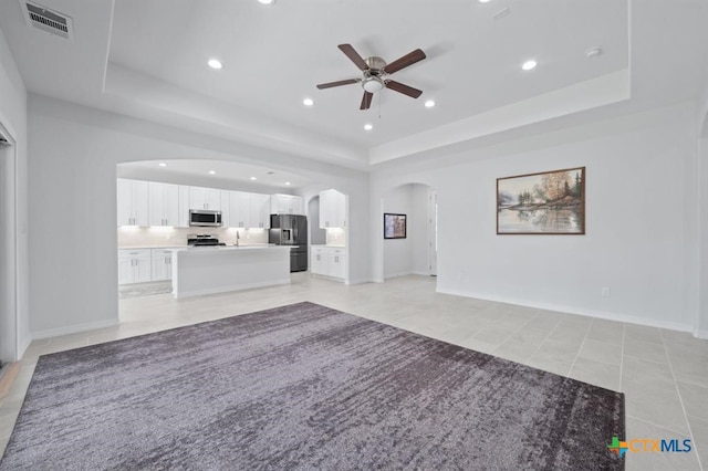 unfurnished living room featuring ceiling fan, light tile patterned flooring, and a raised ceiling