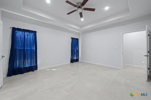 tiled empty room featuring a raised ceiling and ceiling fan