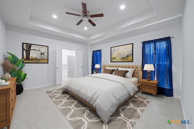 tiled bedroom featuring a tray ceiling, ceiling fan, and ensuite bathroom