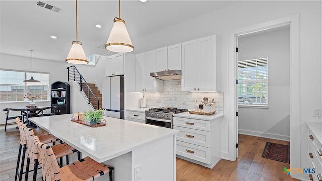 kitchen with white cabinets, white refrigerator, hanging light fixtures, high end stainless steel range, and a kitchen island