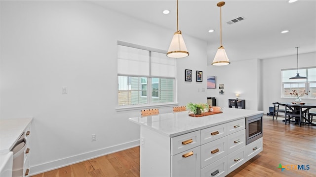 kitchen with light stone countertops, stainless steel microwave, a center island, decorative light fixtures, and white cabinets