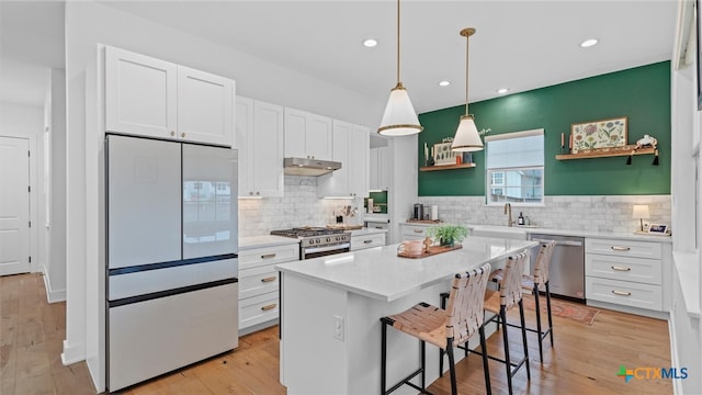 kitchen with hanging light fixtures, white cabinets, a breakfast bar, a kitchen island, and appliances with stainless steel finishes