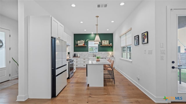 kitchen featuring high quality fridge, a breakfast bar, a kitchen island, decorative light fixtures, and white cabinetry