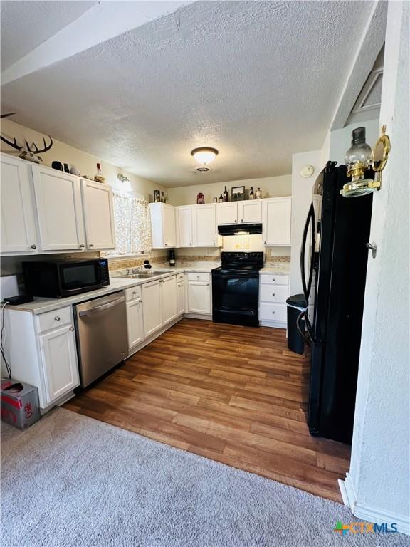 kitchen featuring black appliances, under cabinet range hood, a sink, white cabinets, and dark wood-style flooring