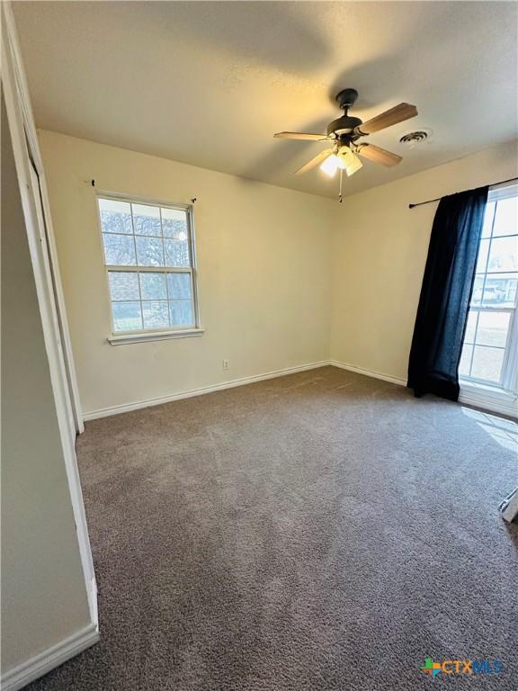 unfurnished room featuring visible vents, carpet flooring, baseboards, and a ceiling fan
