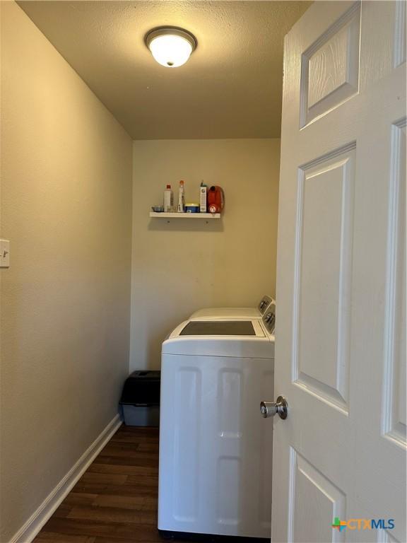 clothes washing area featuring laundry area, baseboards, dark wood-type flooring, and washing machine and clothes dryer