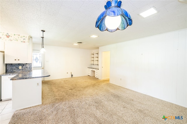 interior space featuring pendant lighting, white cabinets, decorative backsplash, dark stone countertops, and light colored carpet