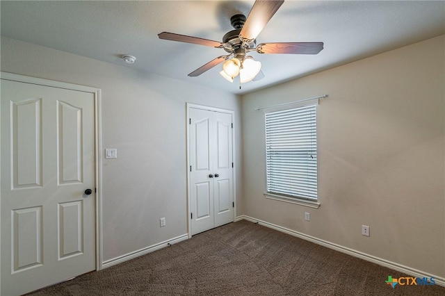 unfurnished bedroom featuring baseboards, a closet, dark carpet, and a ceiling fan