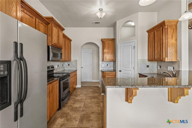 820 Thomas St, Copperas Cove, TX 76522 - kitchen featuring appliances with stainless steel finishes, arched walkways, a peninsula, dark stone counters, and tasteful backsplash