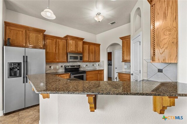 820 Thomas St, Copperas Cove, TX 76522 - kitchen featuring appliances with stainless steel finishes, arched walkways, tasteful backsplash, dark stone countertops, and a peninsula