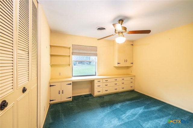 unfurnished bedroom with a ceiling fan, visible vents, dark carpet, and built in study area