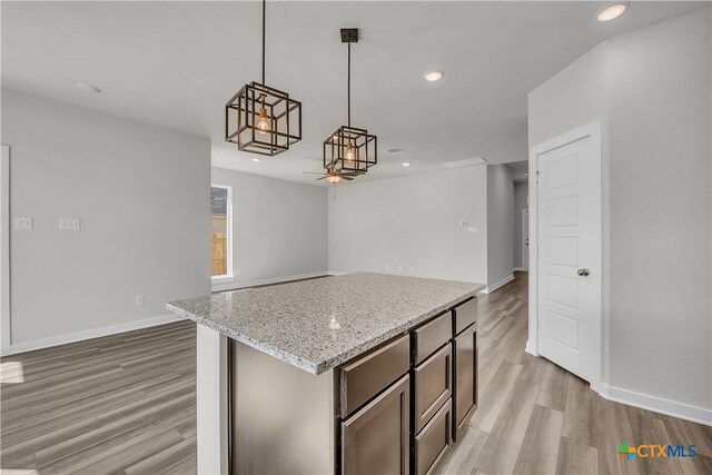 kitchen with a kitchen island, pendant lighting, light stone counters, and light hardwood / wood-style floors