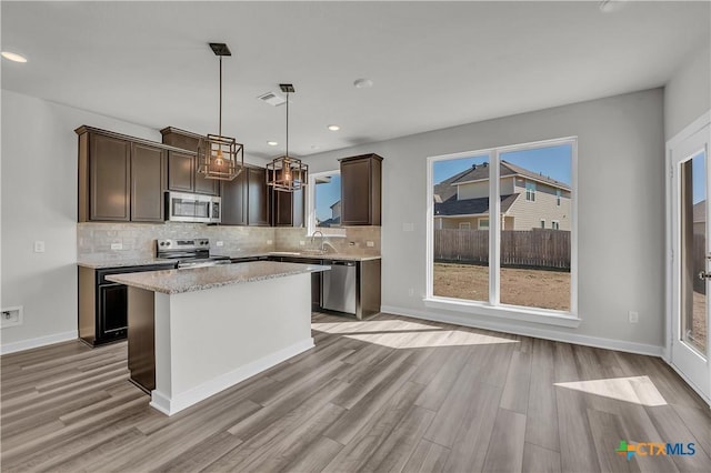 kitchen with stainless steel appliances, a center island, dark brown cabinetry, decorative light fixtures, and light wood-type flooring