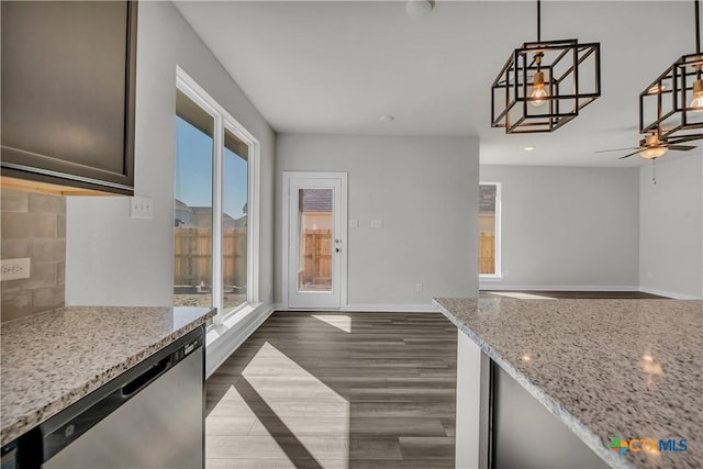 kitchen with a wealth of natural light, decorative light fixtures, dishwasher, light stone counters, and dark wood-type flooring