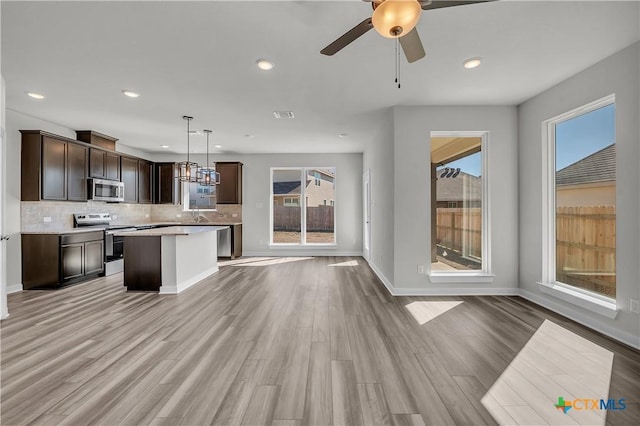 kitchen with appliances with stainless steel finishes, decorative light fixtures, tasteful backsplash, a center island, and light hardwood / wood-style flooring