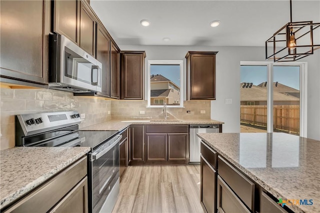 kitchen featuring sink, hanging light fixtures, dark brown cabinets, stainless steel appliances, and light stone counters