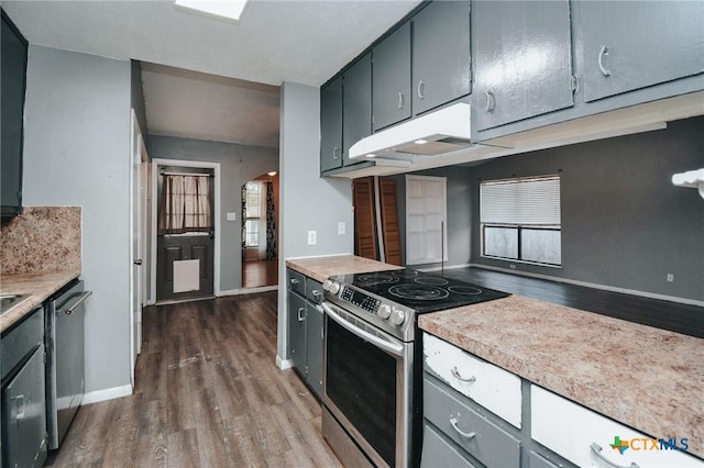 kitchen with arched walkways, under cabinet range hood, stainless steel appliances, light countertops, and dark wood-style floors