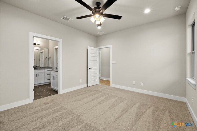 unfurnished bedroom featuring connected bathroom, ceiling fan, and dark colored carpet