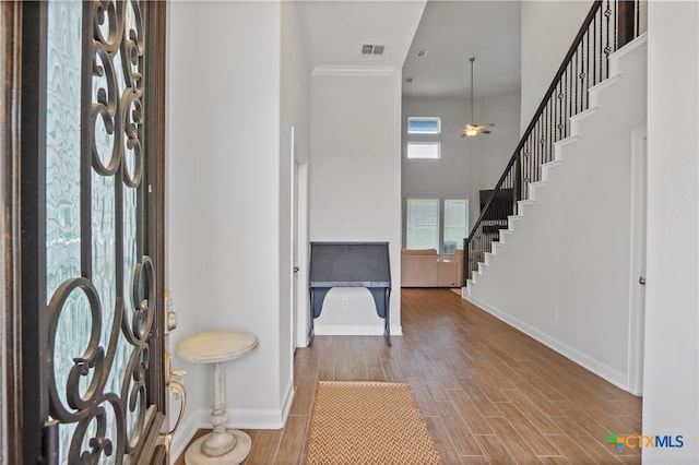 foyer entrance featuring hardwood / wood-style floors, a towering ceiling, ceiling fan, and crown molding