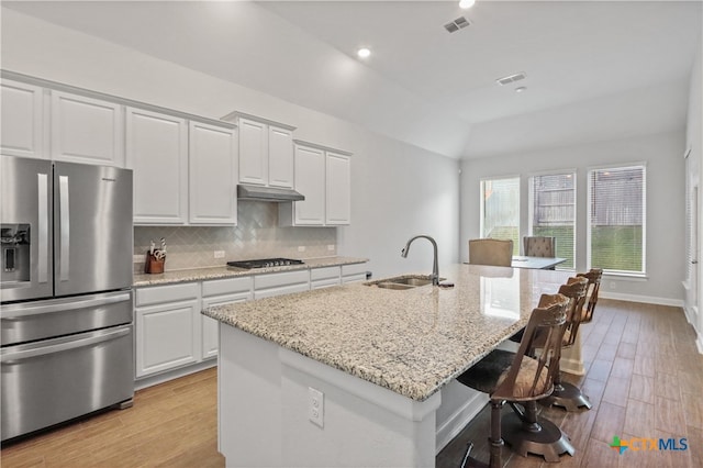 kitchen with stainless steel refrigerator with ice dispenser, a kitchen island with sink, light stone countertops, white cabinetry, and light wood-type flooring