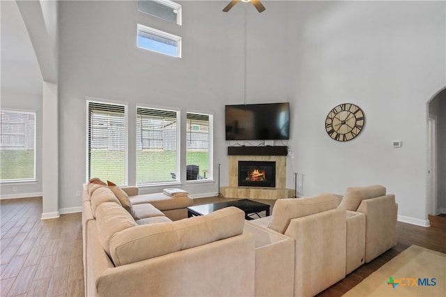 living room featuring a towering ceiling, a fireplace, hardwood / wood-style flooring, and ceiling fan