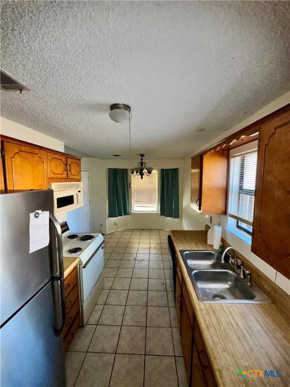 kitchen with white appliances, a textured ceiling, sink, light tile patterned floors, and a notable chandelier