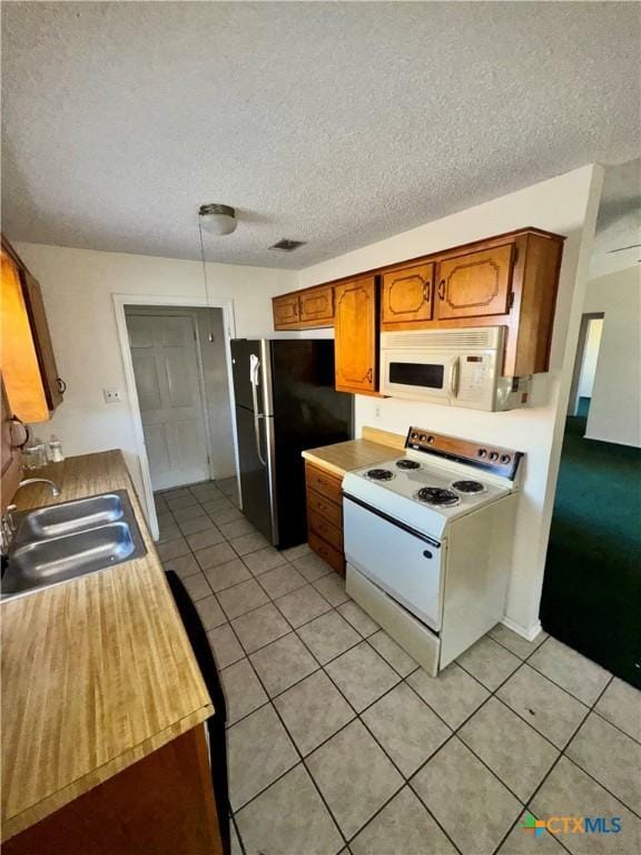 kitchen with a textured ceiling, sink, light tile patterned flooring, and white appliances