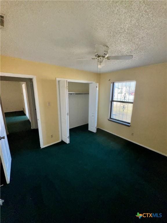 unfurnished bedroom featuring ceiling fan, dark carpet, a textured ceiling, and a closet