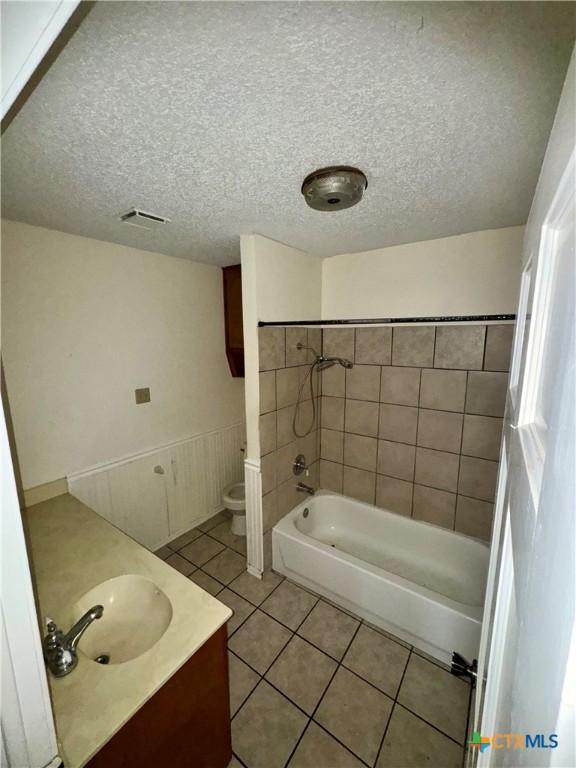 full bathroom with tiled shower / bath combo, tile patterned flooring, a textured ceiling, toilet, and vanity