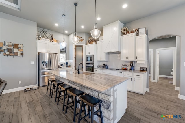 kitchen featuring light wood-type flooring, white cabinetry, appliances with stainless steel finishes, hanging light fixtures, and a kitchen island with sink