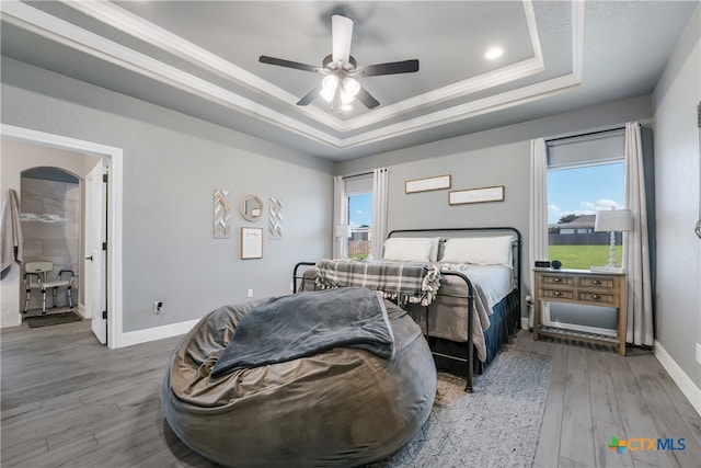 bedroom with light hardwood / wood-style flooring, ceiling fan, and a tray ceiling